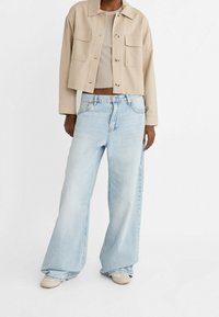 Beige cropped jacket with front pockets, paired with light blue wide-leg jeans. Both pieces in a relaxed fit, denim with faded texture.