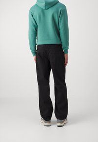 Turkos hoodie med kort design, kombinerad med svarta byxor med lös passform och två bakfickor. Skorna är gråvita.