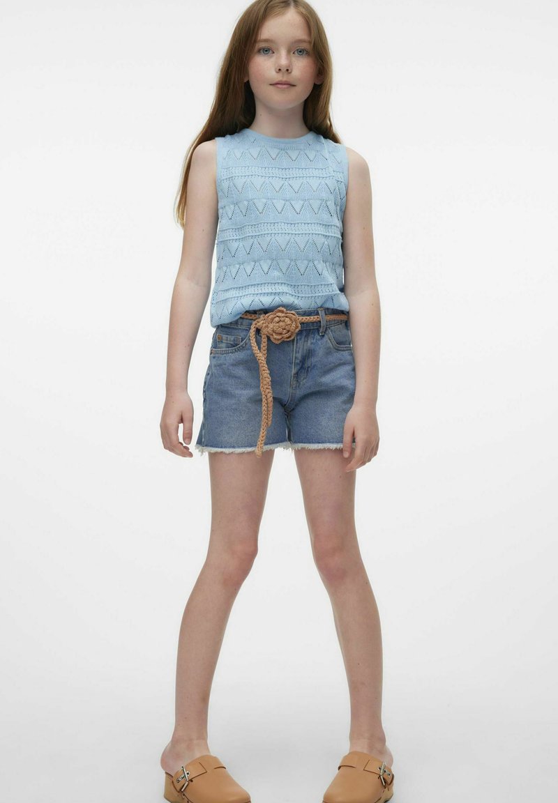 Jasnoniebieski, dzianinowy, bezrękawnik z geometrycznymi wzorami, zestawiony z dżinsowymi szortami i plecionym, brązowym paskiem. Brązowe buty na płaskiej podeszwie.