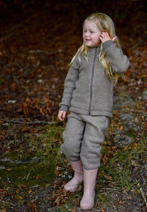 Braune Fleecejacke mit passender Hose, beide mit Reißverschluss und gerippten Bündchen. Pinke Gummistiefel vervollständigen das Outfit.