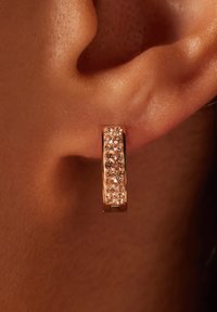 Roze gouden ringoorbel met een gestructureerd oppervlak en kleine heldere kristallen in een rij gezet. Ontworpen om stevig op de oorlel te passen.