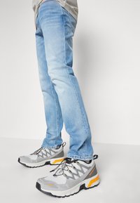 Vaqueros azul claro y botas de senderismo grises con acentos naranjas, que presentan una parte superior texturada, suela flexible y un sistema de cordones.