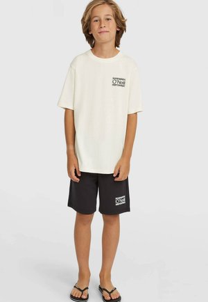 Biele bavlnené tričko s malým čiernym logom na vrecku, v kombinácii s čiernymi šortkami so zodpovedajúcou nášivkou loga. Nosené s čiernymi žabkami.