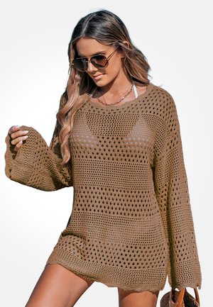 Bruine gebreide cover-up met open geweven patroon, lange mouwen en brede halslijn. Lichte textuur, losse pasvorm en zichtbaar ondergoed eronder.