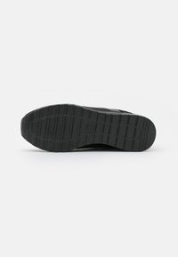 Black sneaker sole with a textured rubber grip pattern, featuring ridges and channels for traction. Includes circular logo detail.