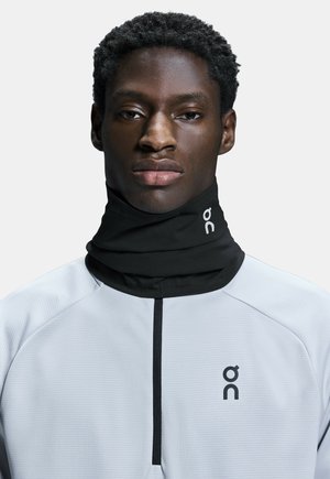 Tour de cou noir associé à un haut de sport gris clair avec un motif texturé et un col zippé. Logo imprimé sur le tissu.