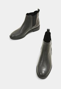 Harmaat nahka nilkkasaappaat, joissa on elastiset sivupaneelit ja teksturoituja yksityiskohtia. Pyöreä kärki ja vetoketju takana. Sileä pinta ja matala korko.