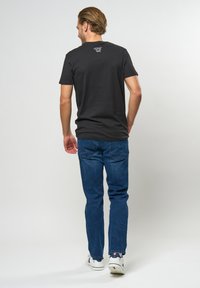 Sort bomulds T-shirt med korte ærmer og et lille logo ved halsen, parret med blå denimjeans og hvide sneakers.