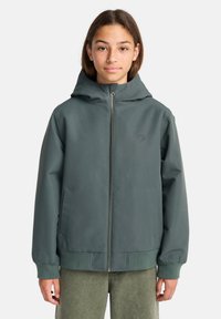 Giacca con cappuccio di colore verde scuro, con zip completa, polsini elasticizzati e tasche laterali. Presenta un logo discreto sul petto e una finitura liscia.