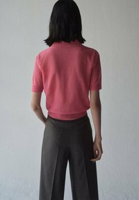 Polo top a maniche corte in maglia rosa con colletto a coste, abbinato a pantaloni scuri grigi a vita alta con gamba larga e tasche visibili.