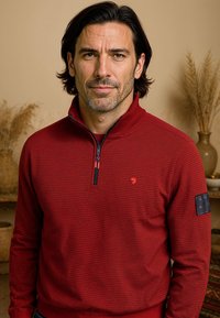 Rood en marineblauw gestreept sweater met een hoge kraag, voorrits en een patch op de linker mouw. Gemaakt van zachte stof met een getailleerd ontwerp.