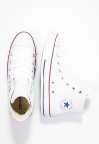 Weiße High-Top-Sneaker aus Canvas mit Metallösen, ausgestattet mit einer Gummisohle, einem roten Streifen und einem runden Logopatch an der Seite.