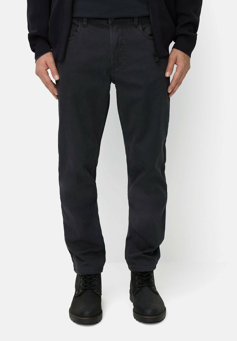 Donker, taps toelopende katoenen broek met een gestructureerde afwerking, voorzien van vijf zakken en riemlussen, gedragen met zwarte veterschoenen.