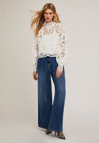 Witte kanten blouse met bloemenpatronen en hoge hals, gecombineerd met hoge taille wijde blauwe spijkerbroek en slangenhuid hoge hakken.