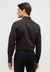 Zwart gestreepte langemouwen shirt met bruine verticale lijnen en een spits kraag, gecombineerd met zwarte broeken met achterzakken.