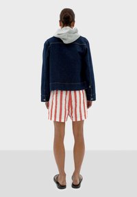 Veste en denim avec capuche grise, shorts rayés rouges et blancs, sandales noires. Vue de dos, design décontracté, coutures et détails en métal visibles.