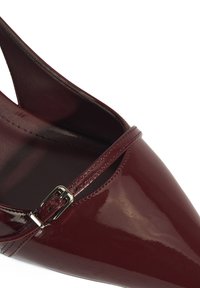 Burgunderfarbene Lackleder-Slingbacks mit spitzem Zehenbereich, verstellbarem Riemen und glänzender Oberfläche, die mit einem metallischen Schnallendetail versehen sind.