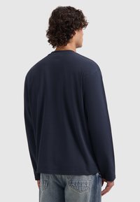 Marineblauwe t-shirt met lange mouwen, gemaakt van zachte stof, met een ronde halslijn en een casual pasvorm, en een naadloos ontwerp aan de achterkant.