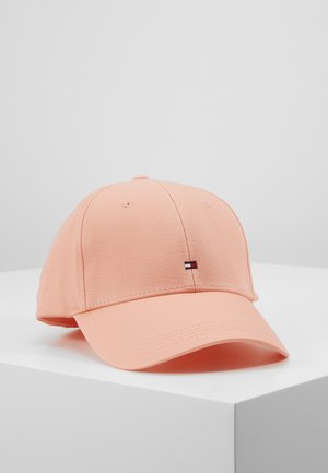Hellrosa Baseballkappe mit kleinem roten, weißen und schwarzen rechteckigen Logo auf der Vorderseite, auf weißer Oberfläche vor grauem Hintergrund dargestellt.