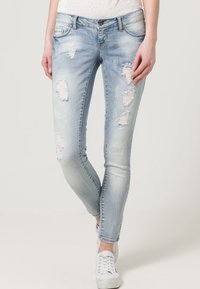 Faded light blue skinny jeans with distressed details and frayed patches. Made from denim, featuring five-pocket styling and a zip fly.