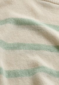 Hellcremefarbener Strickstoff mit sanften grünen horizontalen Streifen und leichten Falten, die Texturdetails zeigen.