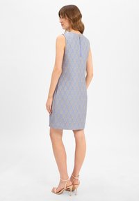 Robe sans manches de couleur bleu clair avec un motif géométrique doré, arrivant au genou, dotée d'un subtil détail de bouton à l'arrière et d'une texture lisse.