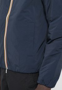 Navy blue lightweight jacket with a zip closure, contrast orange and white zipper, and elastic cuffs. Features a side pocket.