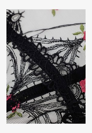 Tissu en dentelle noire avec des motifs floraux complexes et des fleurs brodées roses avec des feuilles vertes sur un fond blanc transparent.