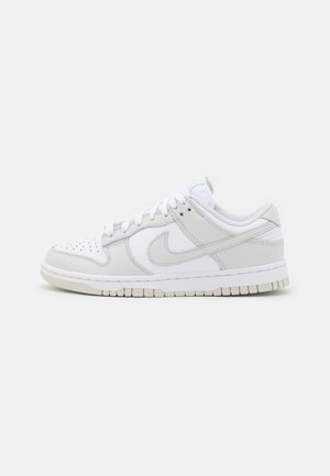 Weißer und hellgrauer Nike Sneaker mit niedrigem Schaft, perforierter Zehenbox und Swoosh-Logo an der Seite, im Profil auf weißem Hintergrund dargestellt.