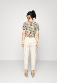Camisola de manga curta com um padrão floral verde, combinada com calças roladas de tom bege claro e mules de salto verde. Conjunto simples e casual.