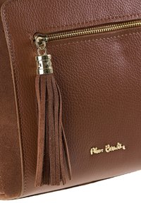 Sezione di borsa in pelle marrone con texture, mostrante una zip dorata con nappina in suede e il logo dorato "Pierre Cardin" sulla superficie.
