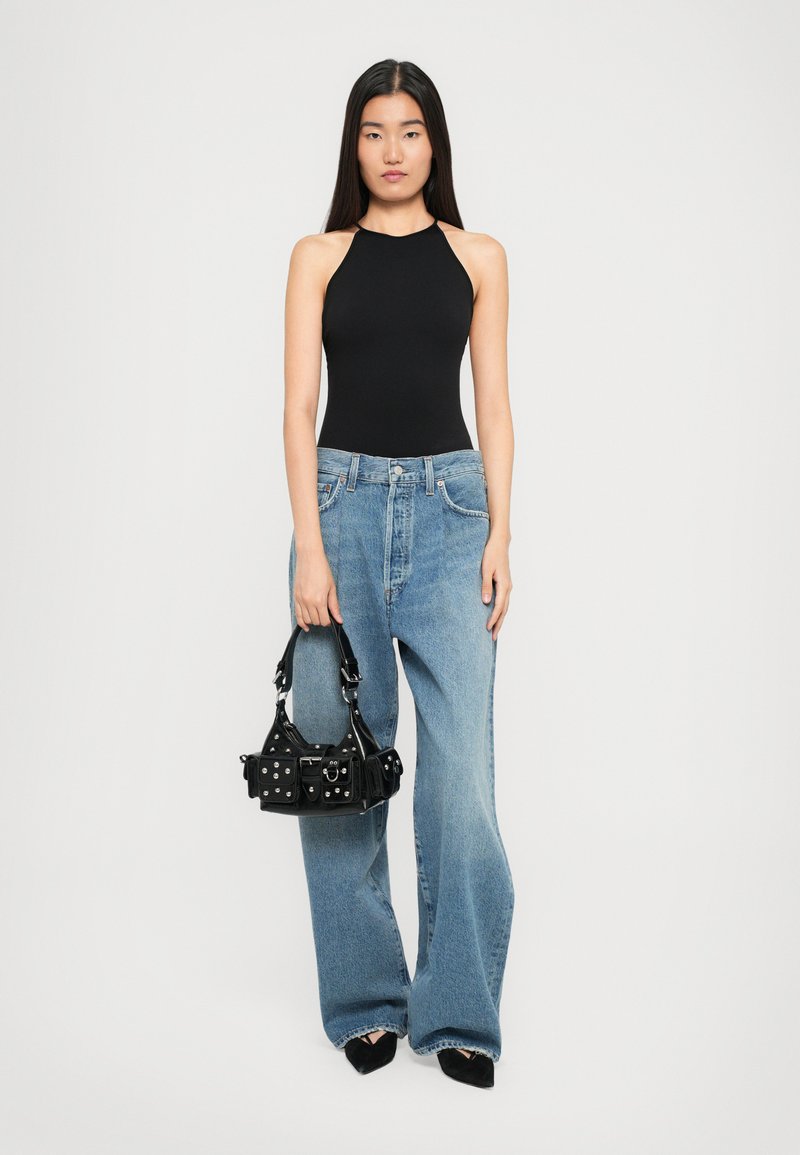 Bodysuit noir sans manches, jeans larges bleu clair, et un petit sac à main noir avec des clous argentés, tenu dans une main.