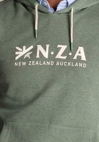 Groen gestreepte hoodie met een voorzak, met de tekst "N.Z.A" en "NEW ZEALAND AUCKLAND" in witte opdruk. De koordjes zijn crème met groene uiteinden.