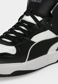 Υψηλή ασπρόμαυρη sneaker Puma με ανάγλυφο δέρμα, μαύρα κορδόνια και παχύ λευκό πέλμα με μαύρη σόλα.
