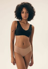 Czarny, bezszwowy biustonosz z szerokimi ramiączkami i głębokim dekoltem w kształcie litery V, w połączeniu z cielistymi majtkami o wysokim stanie. Gładki, elastyczny materiał o prostym wzornictwie.