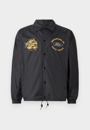 Black windbreaker jacket with ribbed cuffs, snap buttons, and drawstring hem. Features yellow graphic prints of an engine and brand logos.