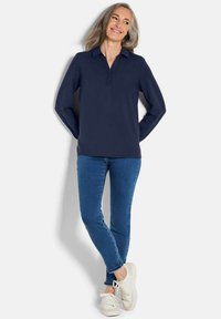 Polo a maniche lunghe blu navy con colletto, dotato di una placca con tre bottoni, abbinato a jeans blu e sneakers bianche.