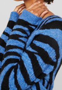 Blå och svart randig tröja med ribbad halsringning och muddar, med mjukt, texturerat tyg och en avslappnad passform.