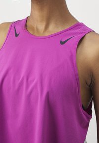 Personne portant un débardeur Nike magenta avec deux logos swoosh noirs près des épaules, haut de la poitrine et cou visibles.