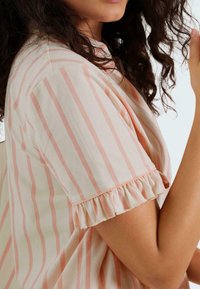 Blouse rayée en mélange de coton doux, avec des rayures horizontales pêche et crème, des bords de manches volantés et une coupe décontractée.