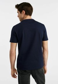Granatowa koszulka z krótkim rękawem, wykonana z miękkiego materiału, z okrągłym dekoltem i lekko teksturowaną powierzchnią. Widok z tyłu pokazuje luźny krój.