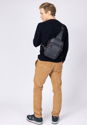 Borsa a tracolla in pelle blu navy con tracolla regolabile, tasca frontale con cerniera e cuciture a contrasto. Texture liscia e forma rettangolare.