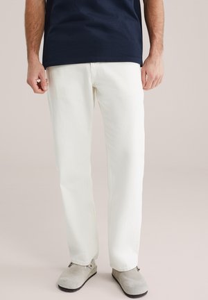 Valged teksapüksid sirge lõikega, millel on sile tekstuur ja minimalistlik disain, kombineeritud hallide seemisnahast kingadega.