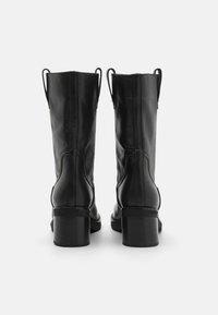 Mustat nahkaiset nilkkurit, joissa on sileä pinta, pyöreät kärjet ja paksut korot. Varustettu saumanompeleilla ja vetolenkeillä kannassa.