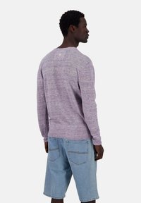 Pullover-Strickpullover in hellem Lila mit gerippten Bündchen und Saum. Kombiniert mit blauen Jeansshorts und minimaler Branding-Ausstattung auf der Rückseite.