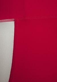 Tissu athlétique rouge avec un panneau contrastant gris clair. Texture lisse, coutures plates et design globalement ajusté.