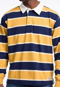 Yellow and navy striped long-sleeve polo shirt with a white collar, featuring a front placket and woven label on the hem.