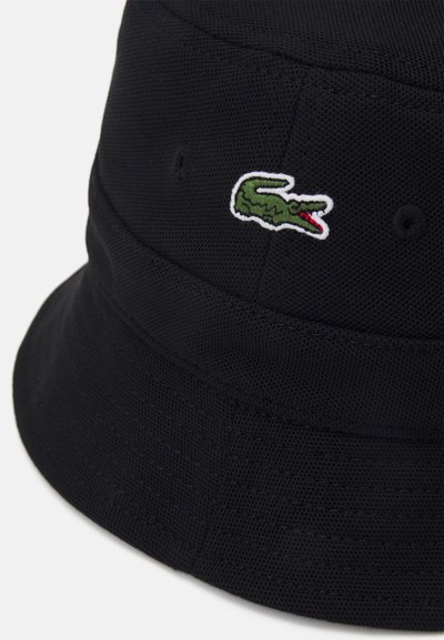 Chapeau seau noir en tissu texturé, arborant un logo de crocodile vert brodé sur le côté. Forme ronde avec un large bord incliné vers le bas.