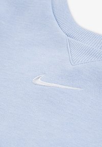 Light blue sweatshirt made of soft fabric, featuring a white embroidered Nike logo on the front and a textured neckline detail.