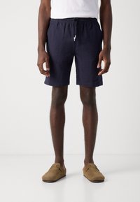 Marineblauwe zwemshorts met elastische taille en textuurpatroon, voorzien van zijzakken, gecombineerd met bruine suède instap schoenen.